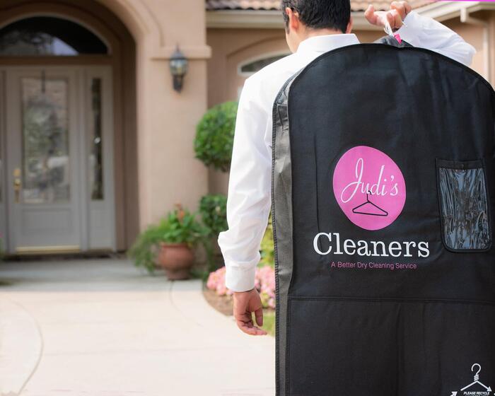 Man walking with dry cleaning branded with Judi's Cleaners logo